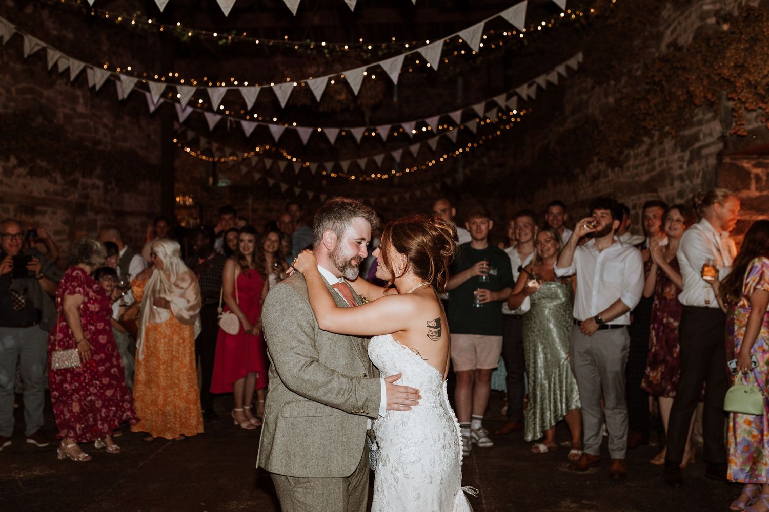 Couples first dance together under string lights and bunting decorations at an evening reception celebration.