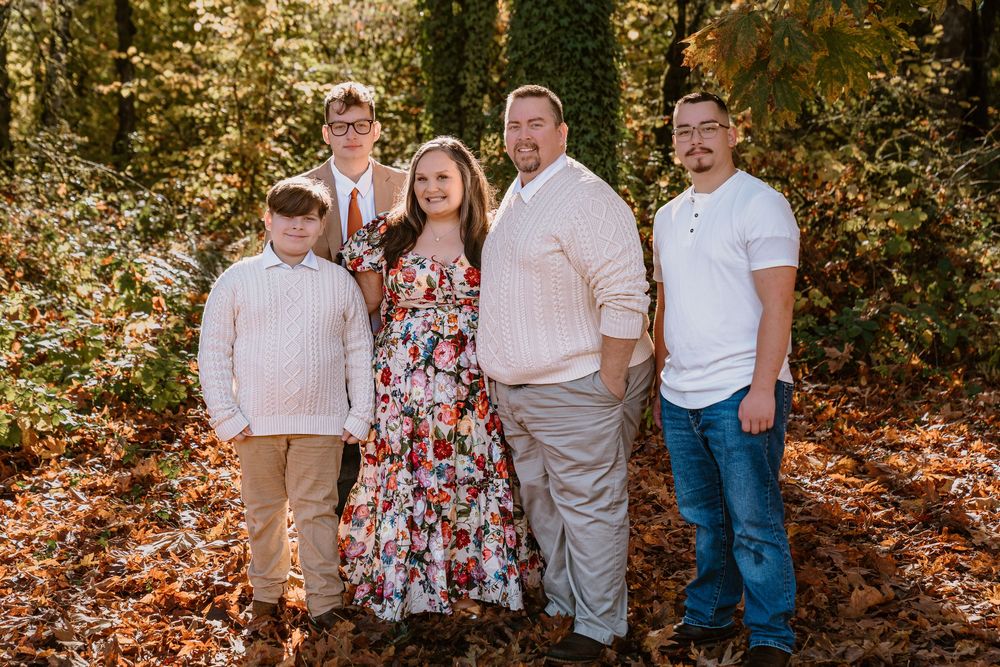 Family of five posing outdoors among autumn leaves and trees during a fall family portrait session.