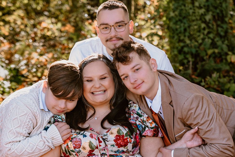 Happy family of four posing outdoors, smiling together among green foliage in a warm, candid portrait.