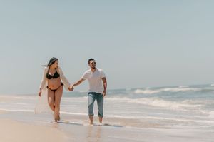 Couple holding hands while walking along a sandy beach with ocean waves in the background.