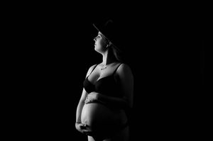 Silhouetted figure in athletic wear stands against dark background during pregnancy photoshoot.