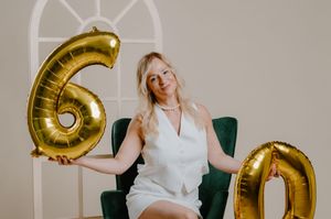 Woman in white dress poses with large gold number balloons during celebratory photoshoot.