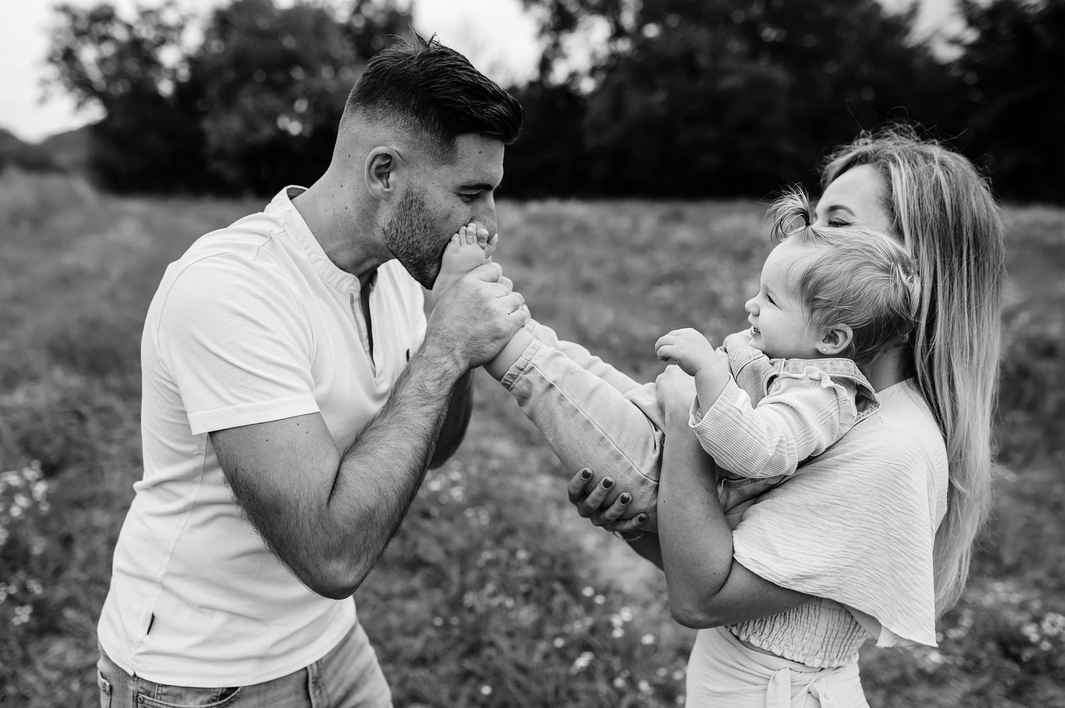 A black and white photo series showing a family playfully blowing bubbles together in an outdoor setting.