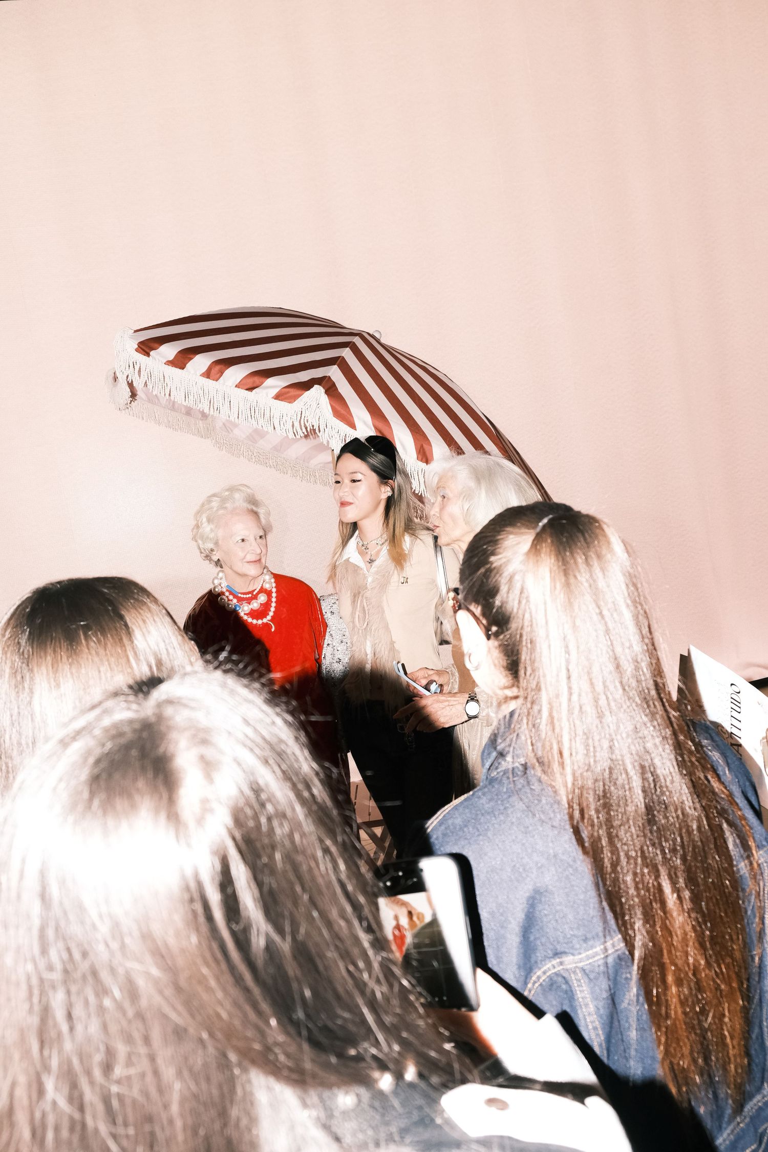 A group of people gather under a red and white striped parasol at a social event in vintage style photography.