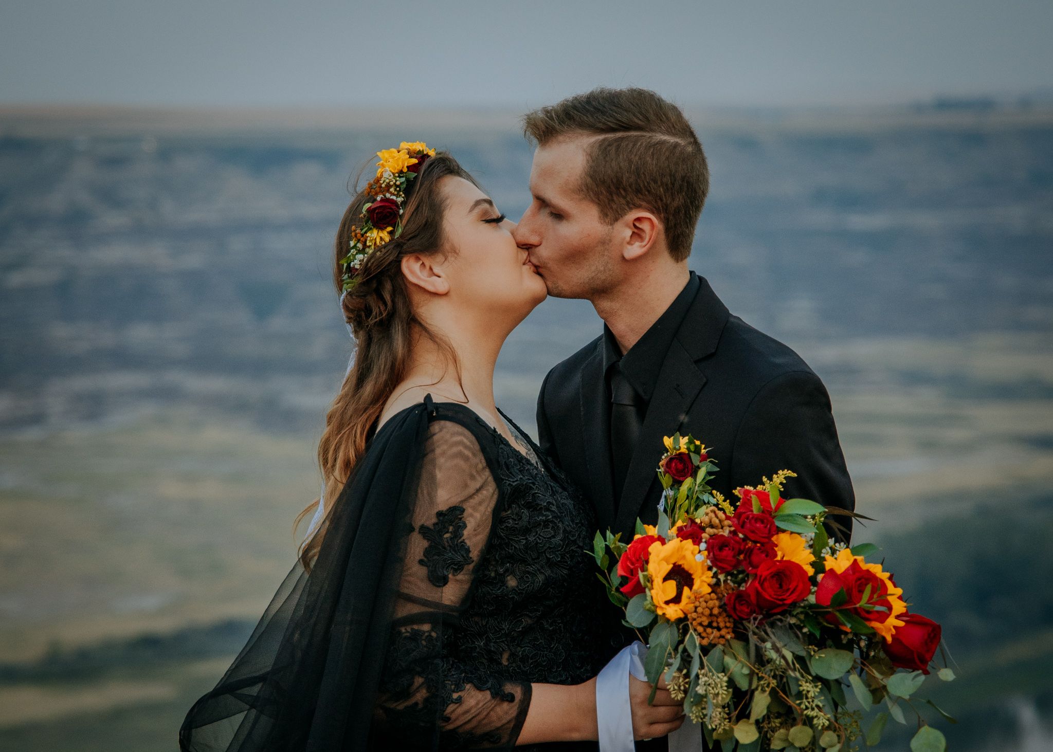 A couple shares a romantic moment against a scenic mountain landscape at sunset.