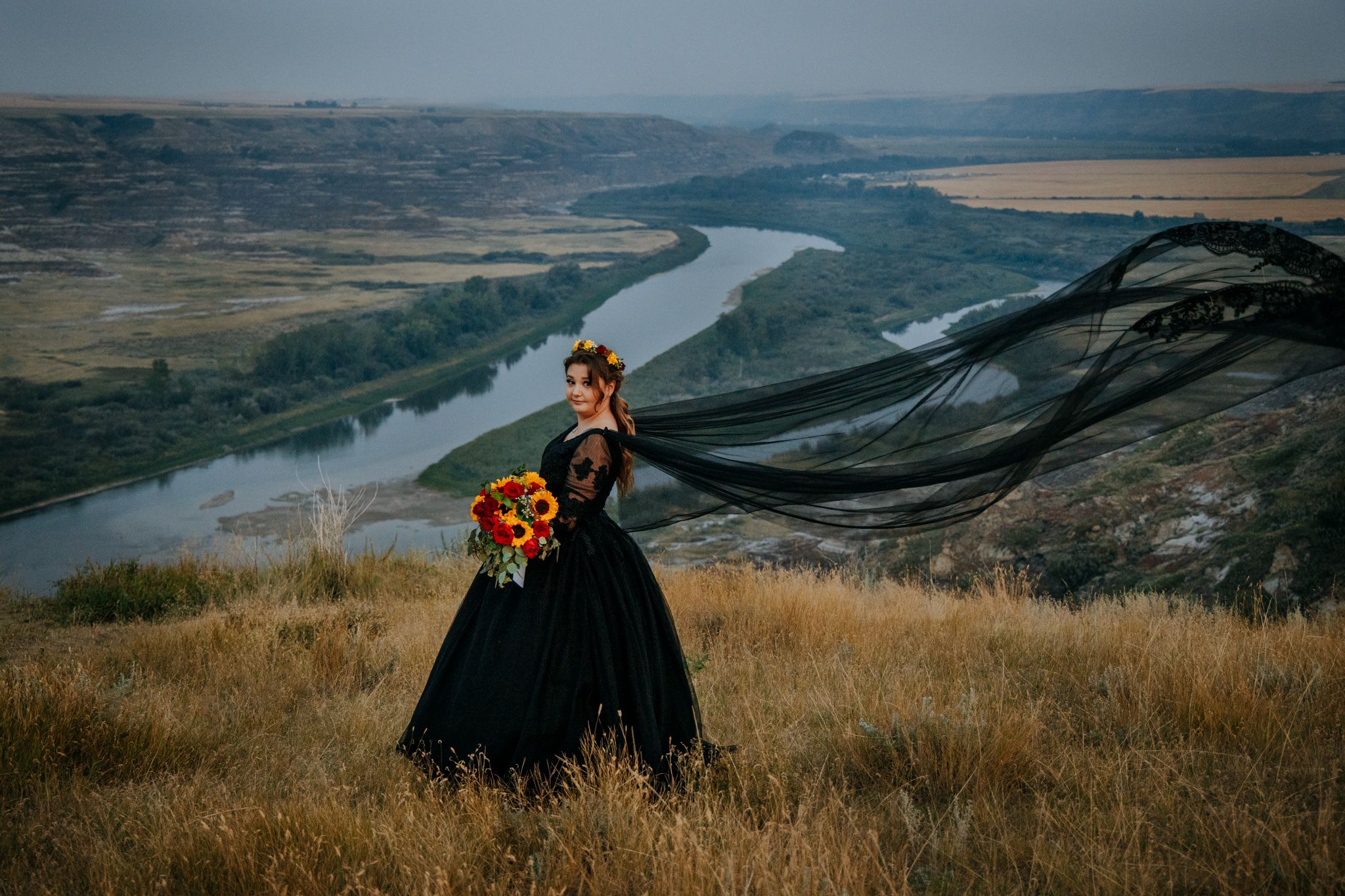 Scenic panoramic view of a winding river valley with golden grass and dramatic overcast skies in the background.