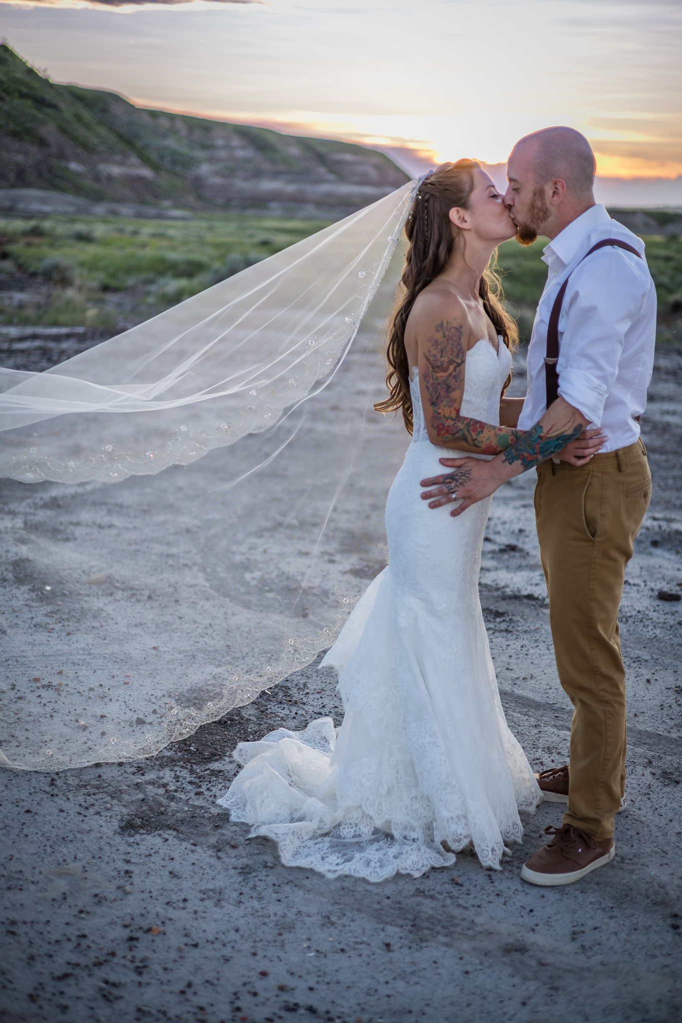 A romantic sunset wedding photo series shows a couple embracing on rocky terrain with a flowing white veil catching the breeze.