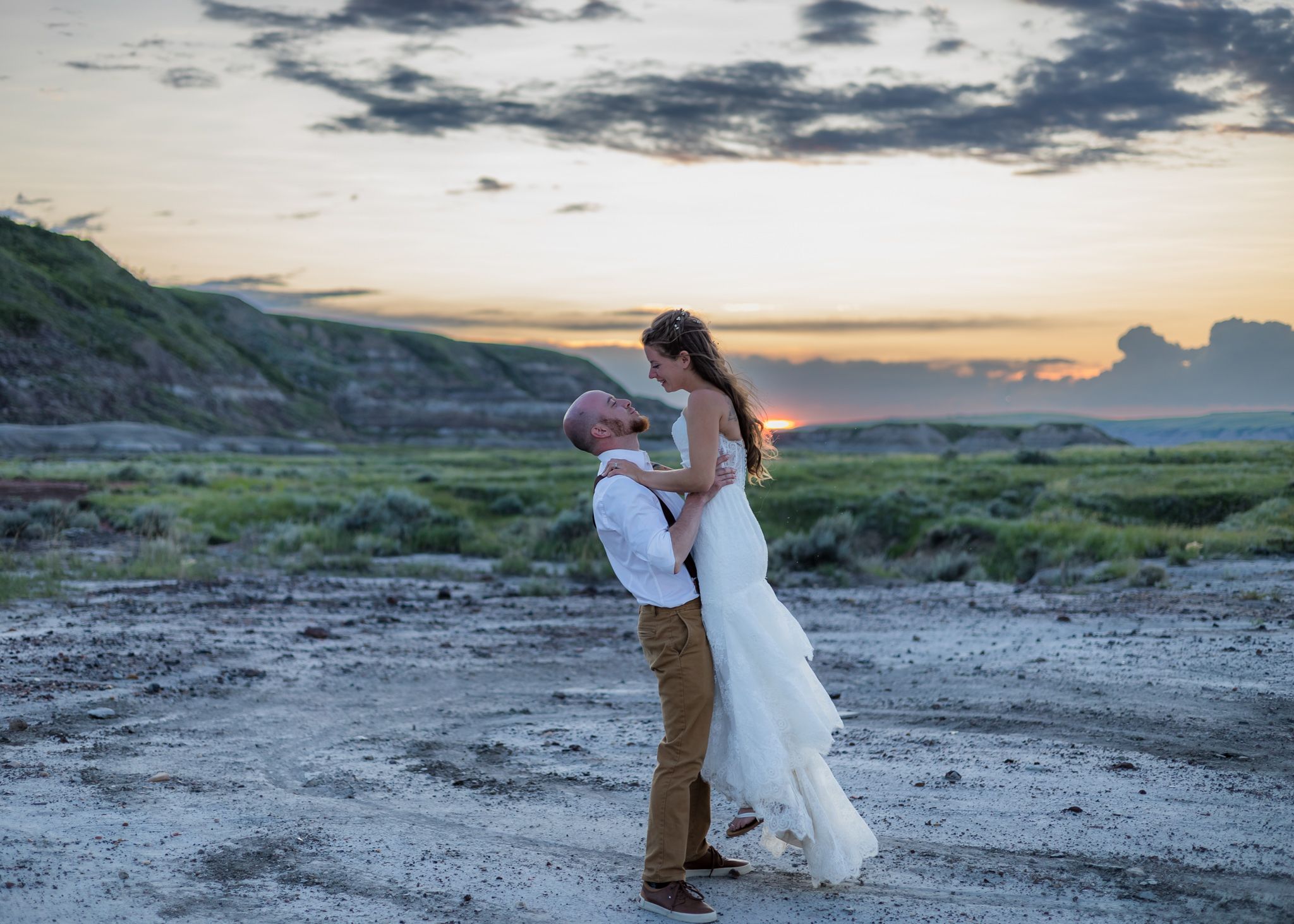 A couple shares an intimate moment on a rocky beach at sunset as waves crash against the shore.