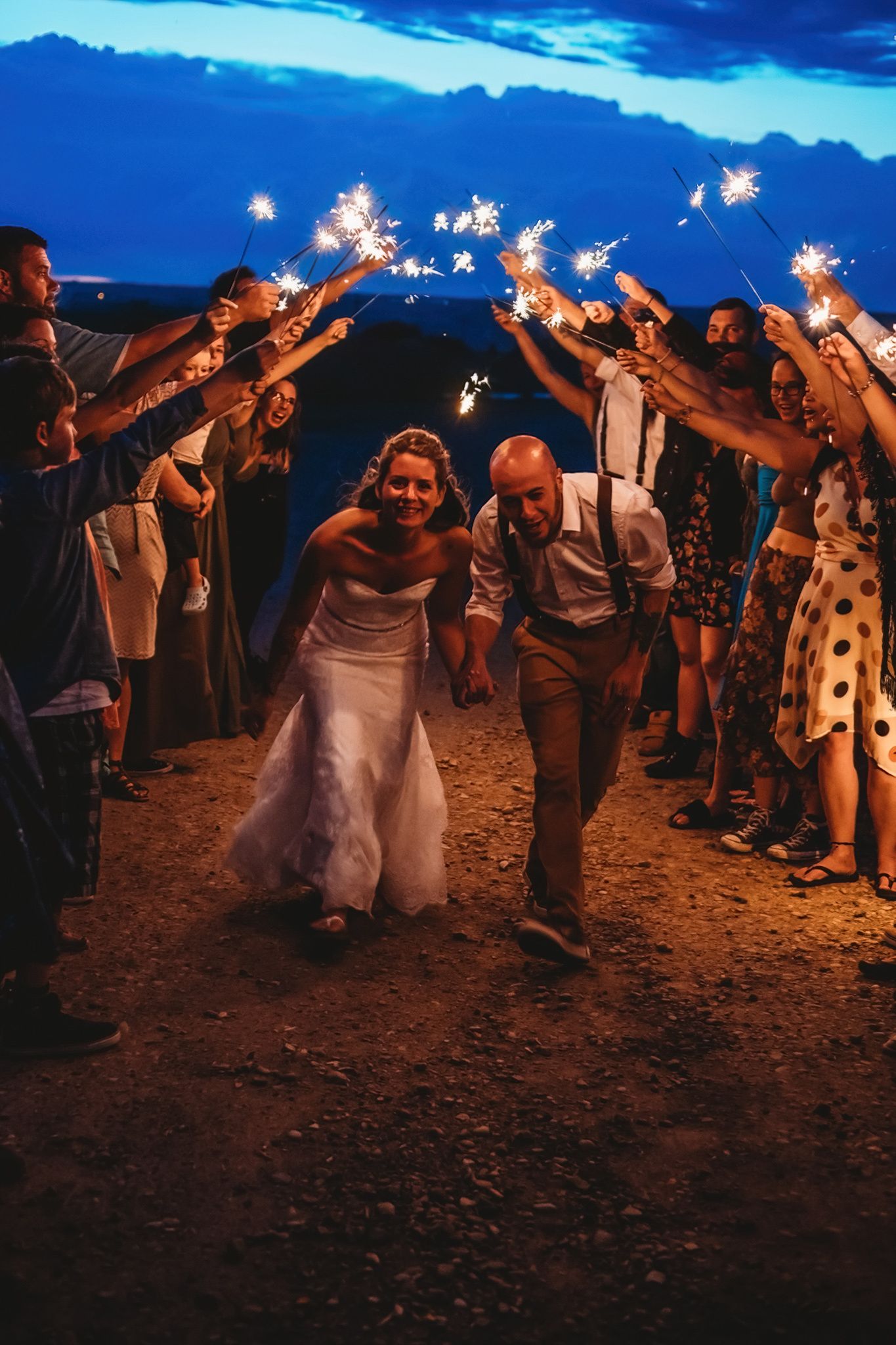 Wedding guests form a sparkler tunnel exit at dusk as newlyweds walk through during outdoor evening celebration.