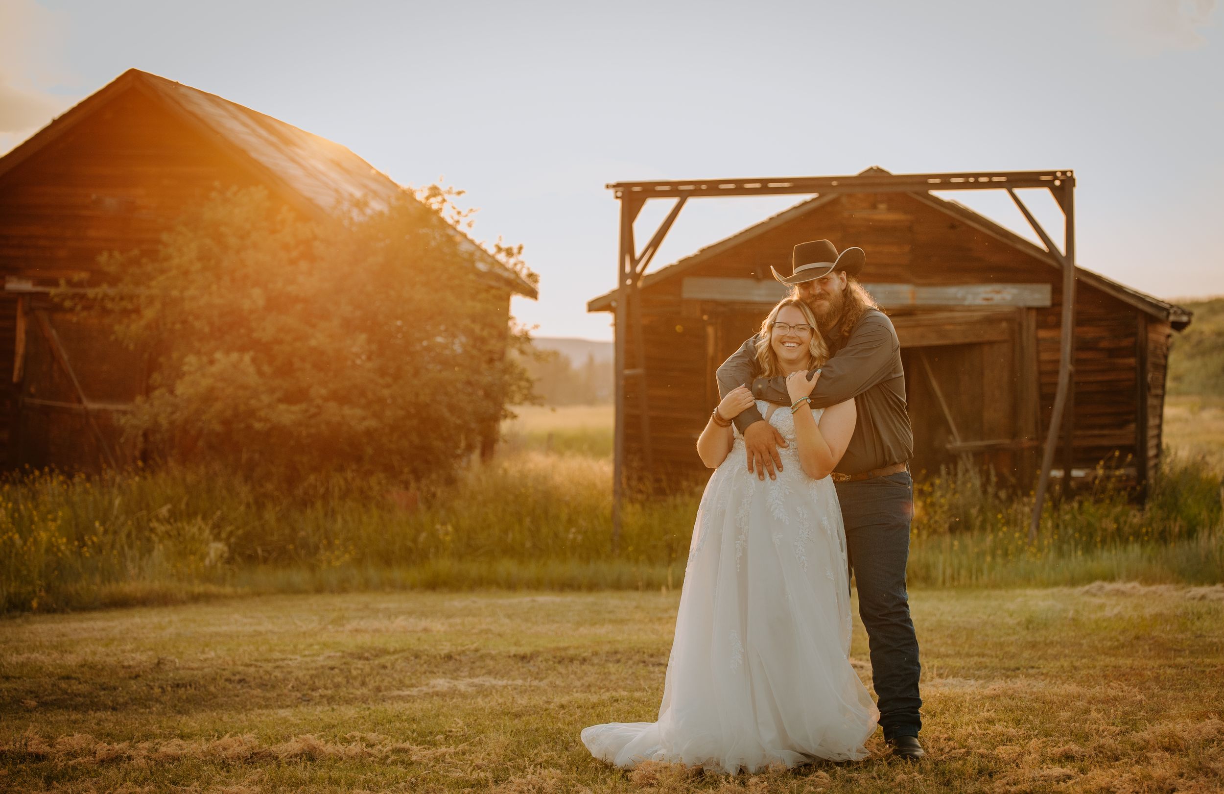 A couple shares an intimate moment in front of a rustic barn during golden hour.