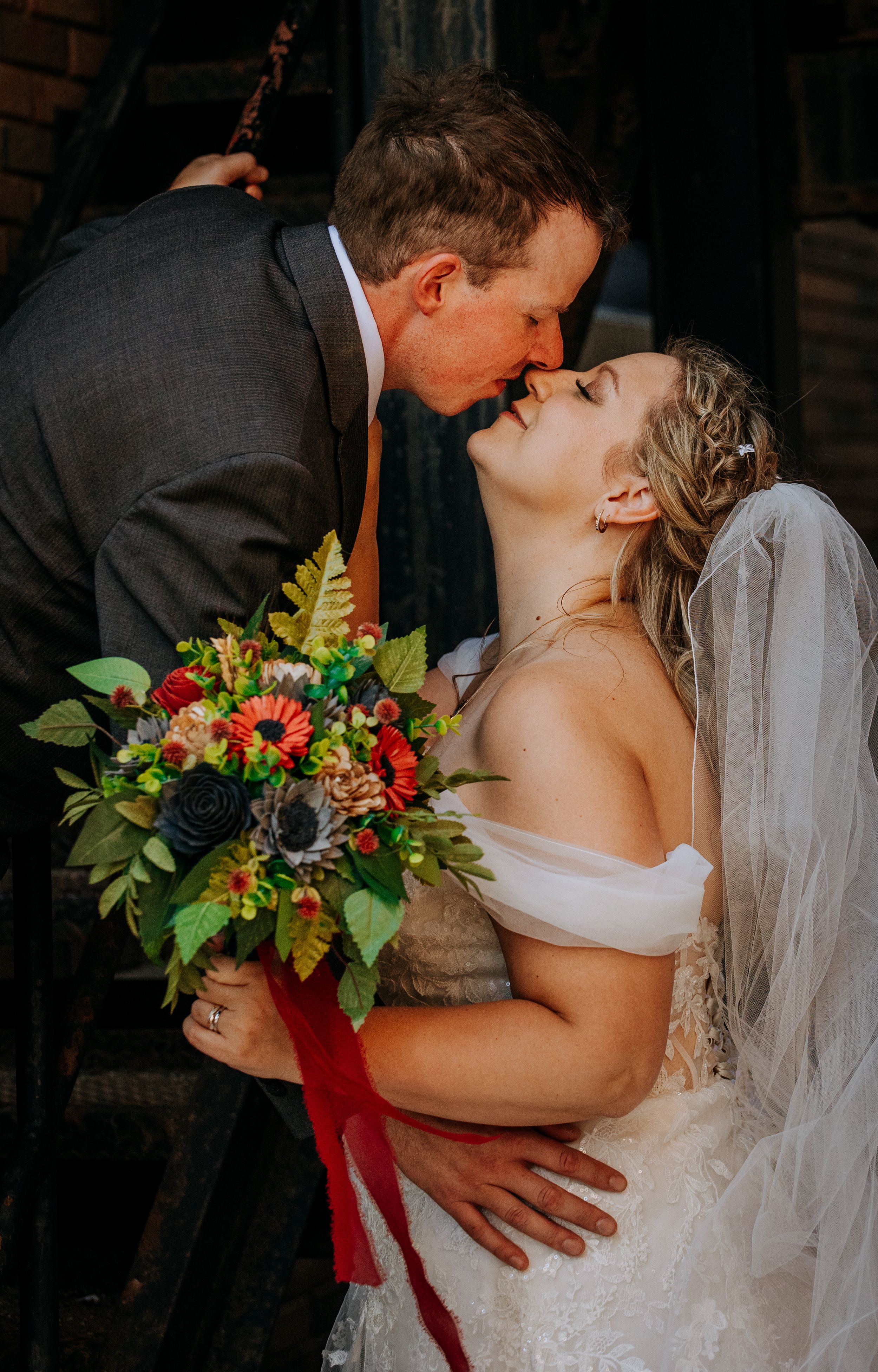 A romantic wedding photo series showing tender moments between newlyweds with a vibrant red floral bouquet.
