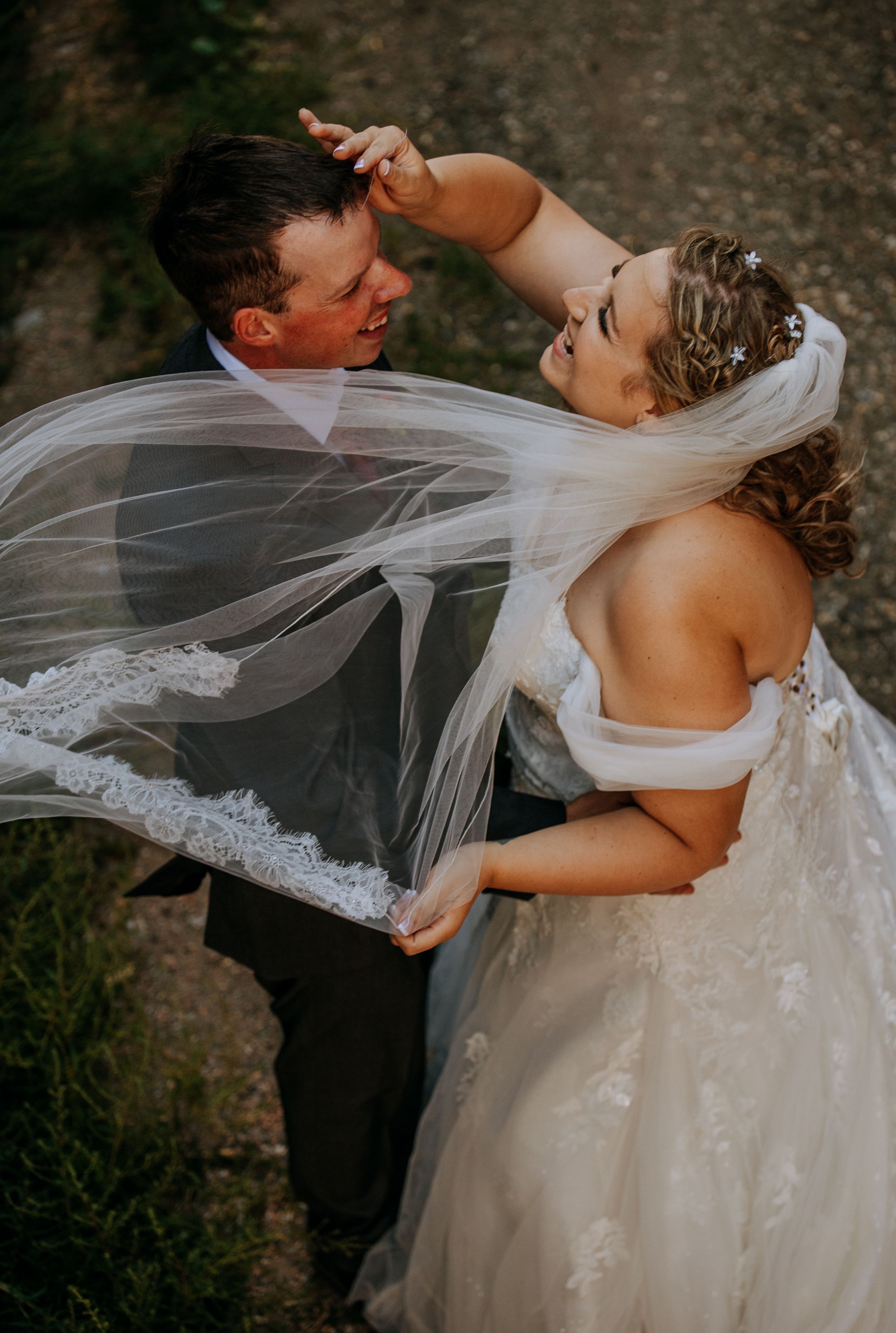 A joyful wedding couple dancing together outdoors as the bride's delicate lace veil flows in the breeze.