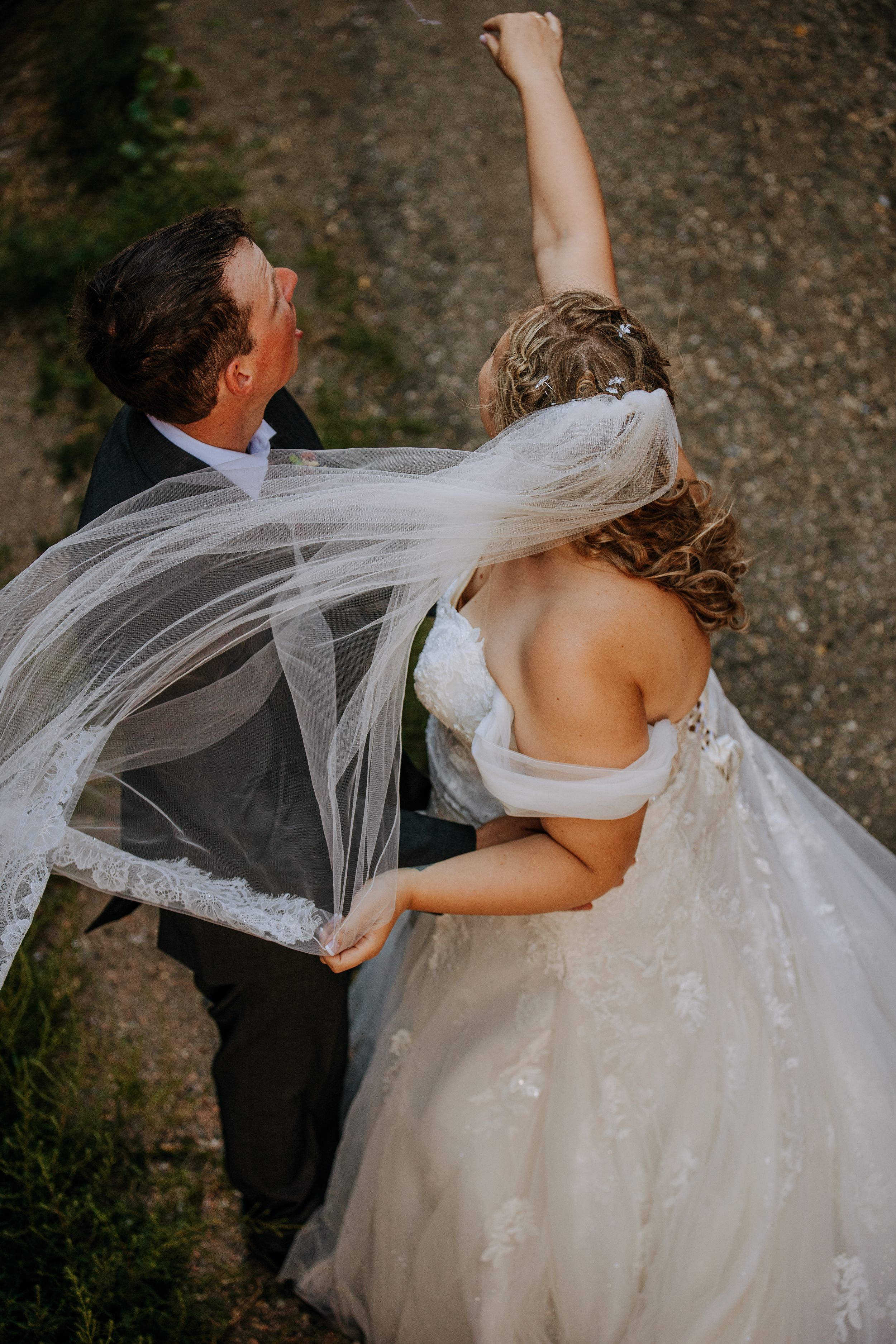 A couple celebrates their wedding day with the bride's veil flowing in the wind as they raise their arms in joy.