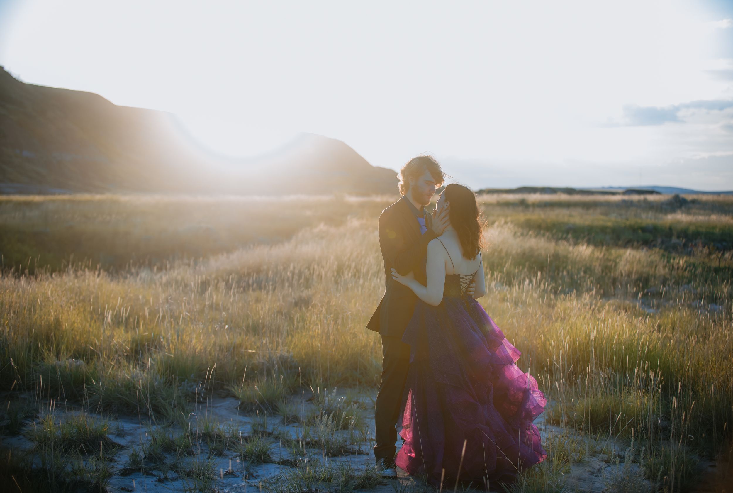 Silhouettes of two people embracing in a golden field at sunset with sunlight streaming through the scene.