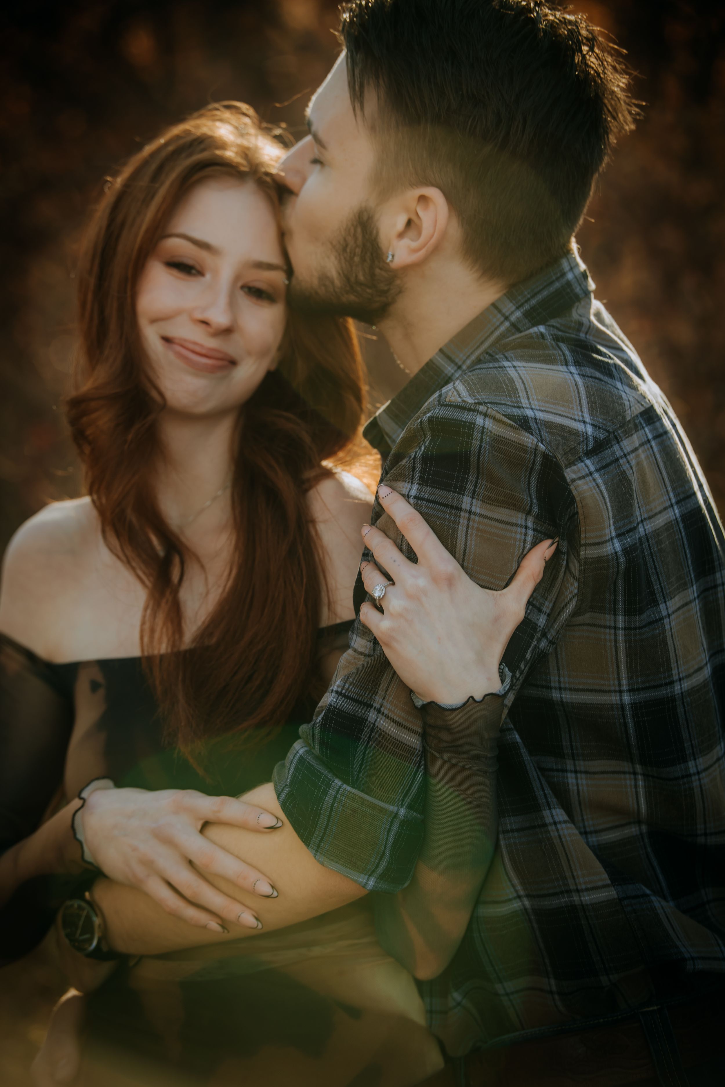 Romantic couple embraces during golden hour sunset photoshoot, with warm backlighting creating a dreamy atmosphere.