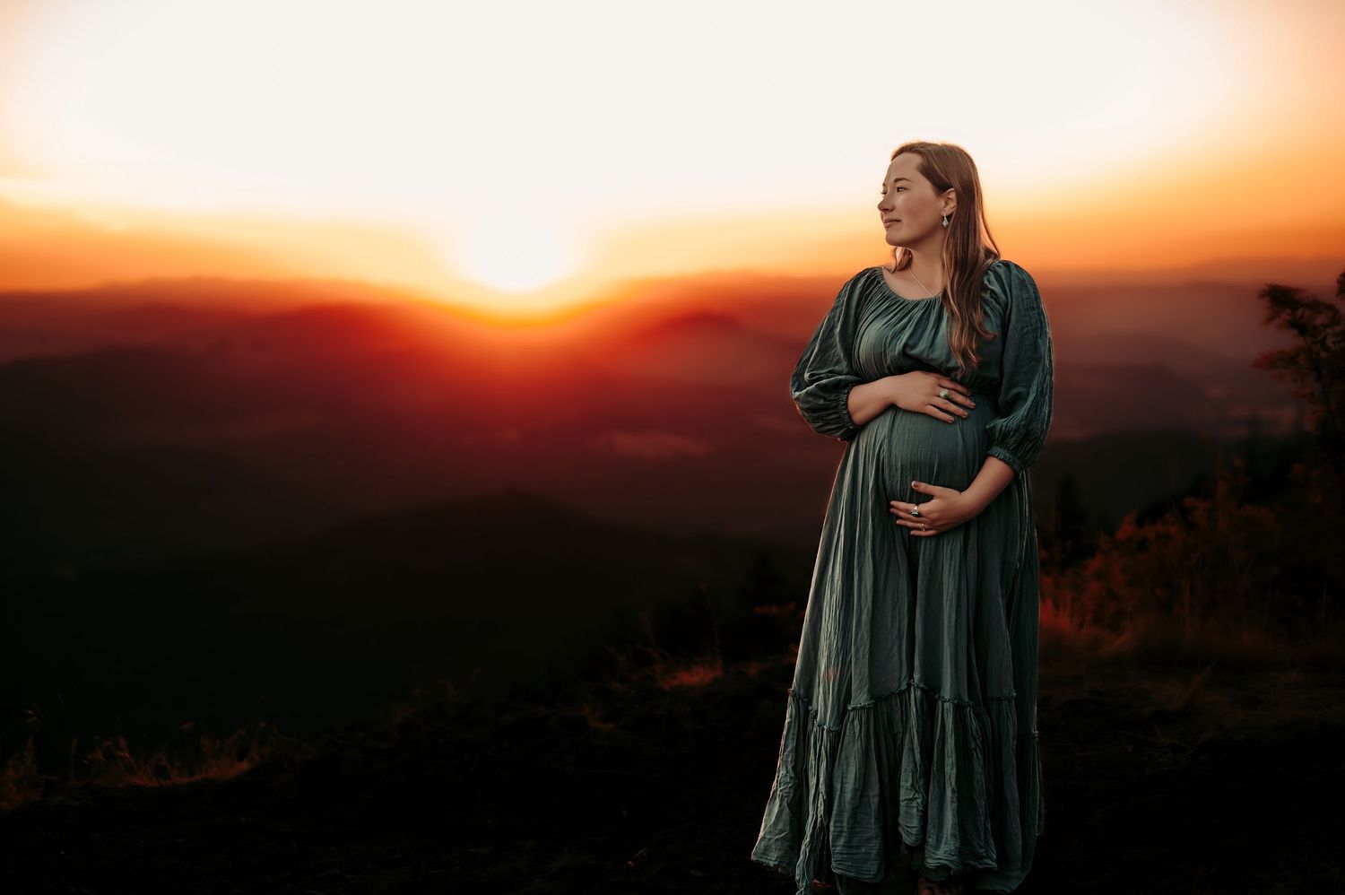 Silhouette of an expectant mother in a flowing dress against a dramatic sunset.