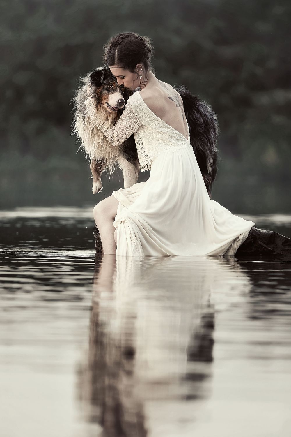 A person in a flowing white dress sits gracefully in dark water creating a dreamy artistic reflection.