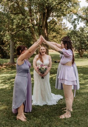 Bridal party in pastel dresses creates fun high-five poses in outdoor garden setting.