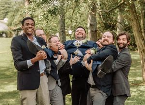 Wedding party members create candid moments during an outdoor photography session among trees.