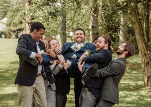 Groomsmen create a fun photo moment together while celebrating outdoors among trees.