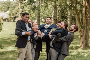 Wedding party members share laughter while posing for candid photos in a natural outdoor setting.