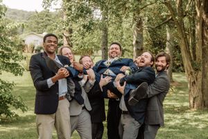 Groomsmen share jovial moments while taking group photos in a natural outdoor setting.