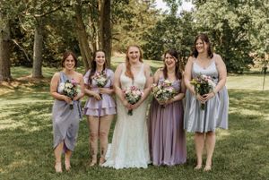 Wedding party members gather outdoors wearing coordinated purple and gray dresses.