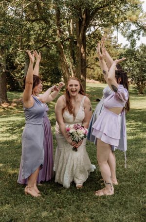 Wedding party members jump and celebrate with enthusiasm in outdoor garden setting.