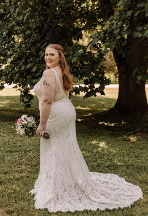 A beautiful white lace wedding dress with intricate details photographed in natural outdoor lighting.