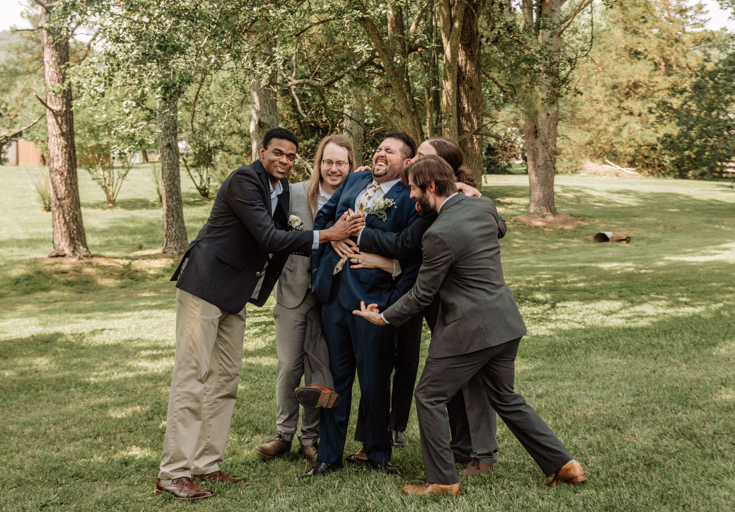 Candid group photo of wedding party having fun outdoors in a park setting.