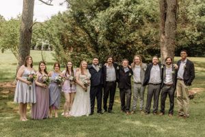 Wedding party group photo with bridesmaids and groomsmen lined up in outdoor garden setting.