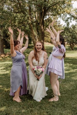 Bridal party creates energetic celebration poses on grass under trees.