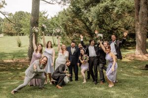 Wedding group lounges casually on green grass during outdoor photo session.