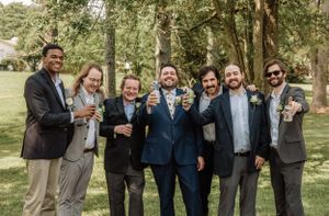 Groomsmen in suits and sunglasses pose playfully for informal photos in a park setting.