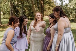 Wedding party in coordinated purple and gray attire poses together outdoors.