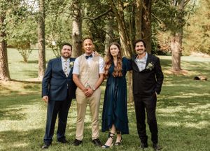Group wedding photo showing wedding party lined up outdoors in formal attire under trees.
