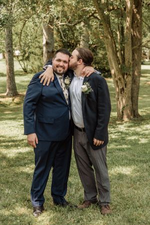 Three groomsmen share a lighthearted moment together on a sunny day in a park setting.