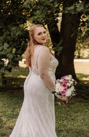 Elegant white lace wedding gown showcased in an outdoor setting with natural lighting.