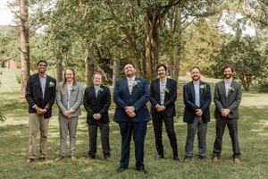 Formal group photo of groomsmen wearing navy and gray suits in park setting.