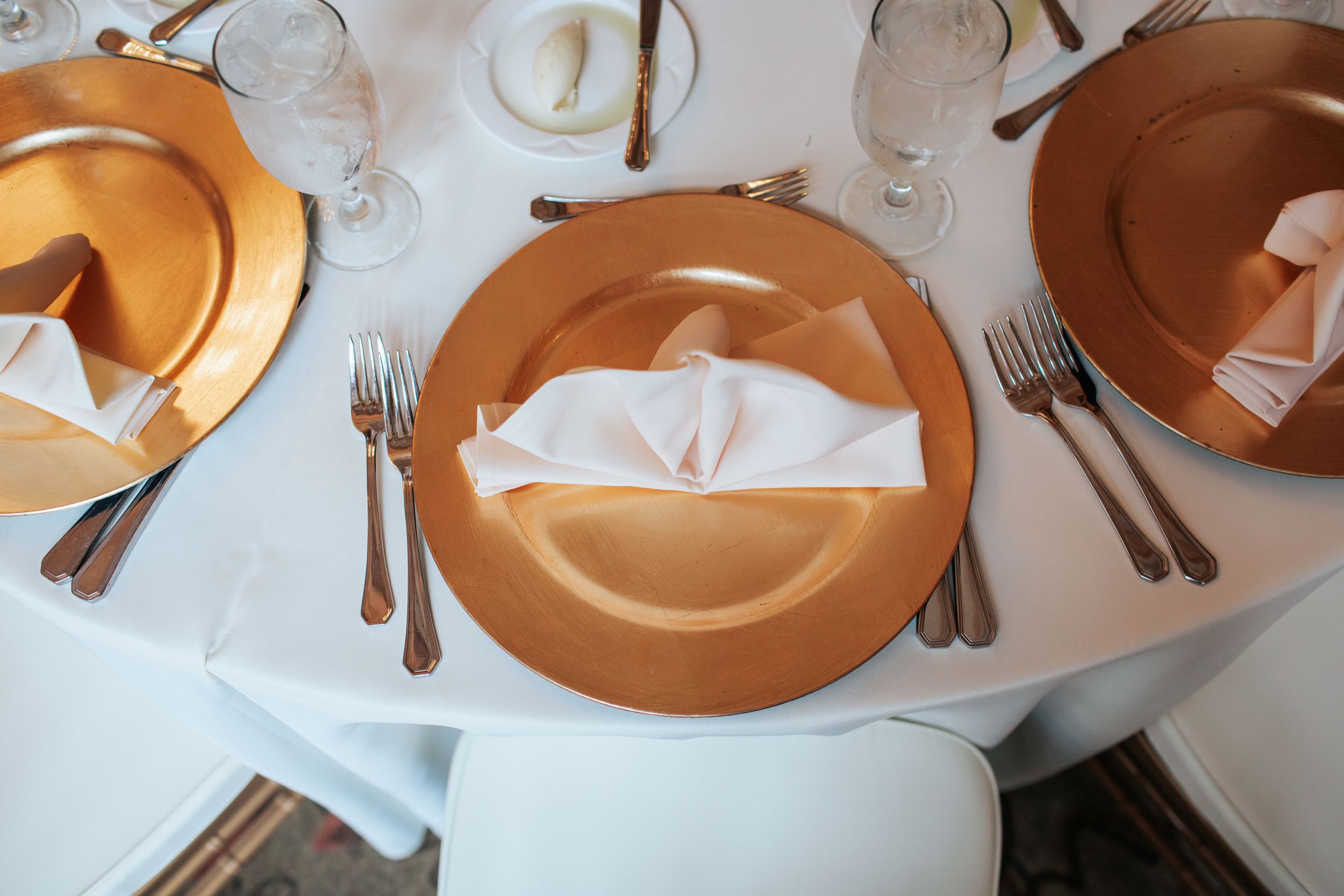 Orange and white place settings with silverware arranged on a formal dining table with white tablecloth.