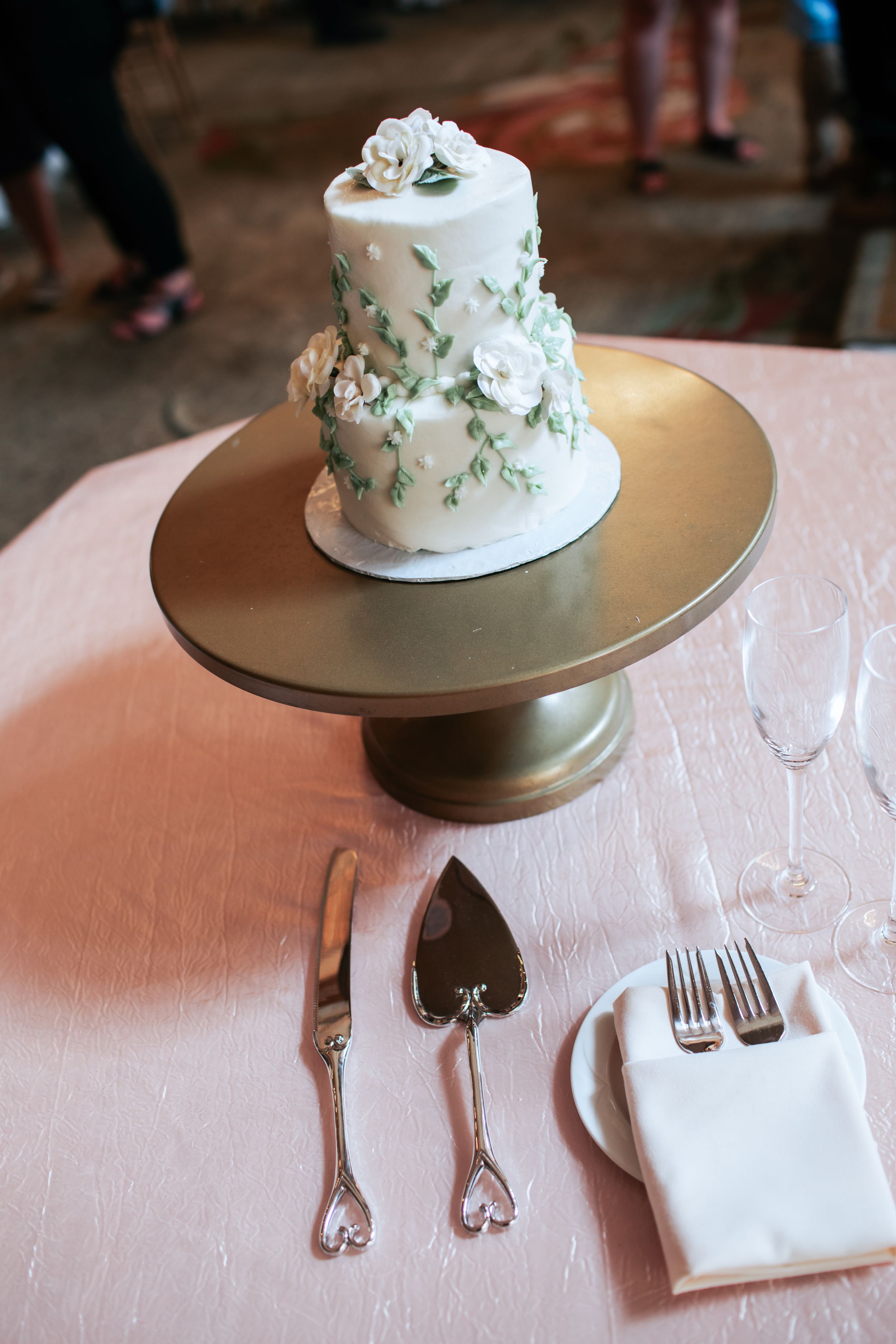 Three elegant place settings with white linens and silverware display a small white wedding cake with floral decorations.