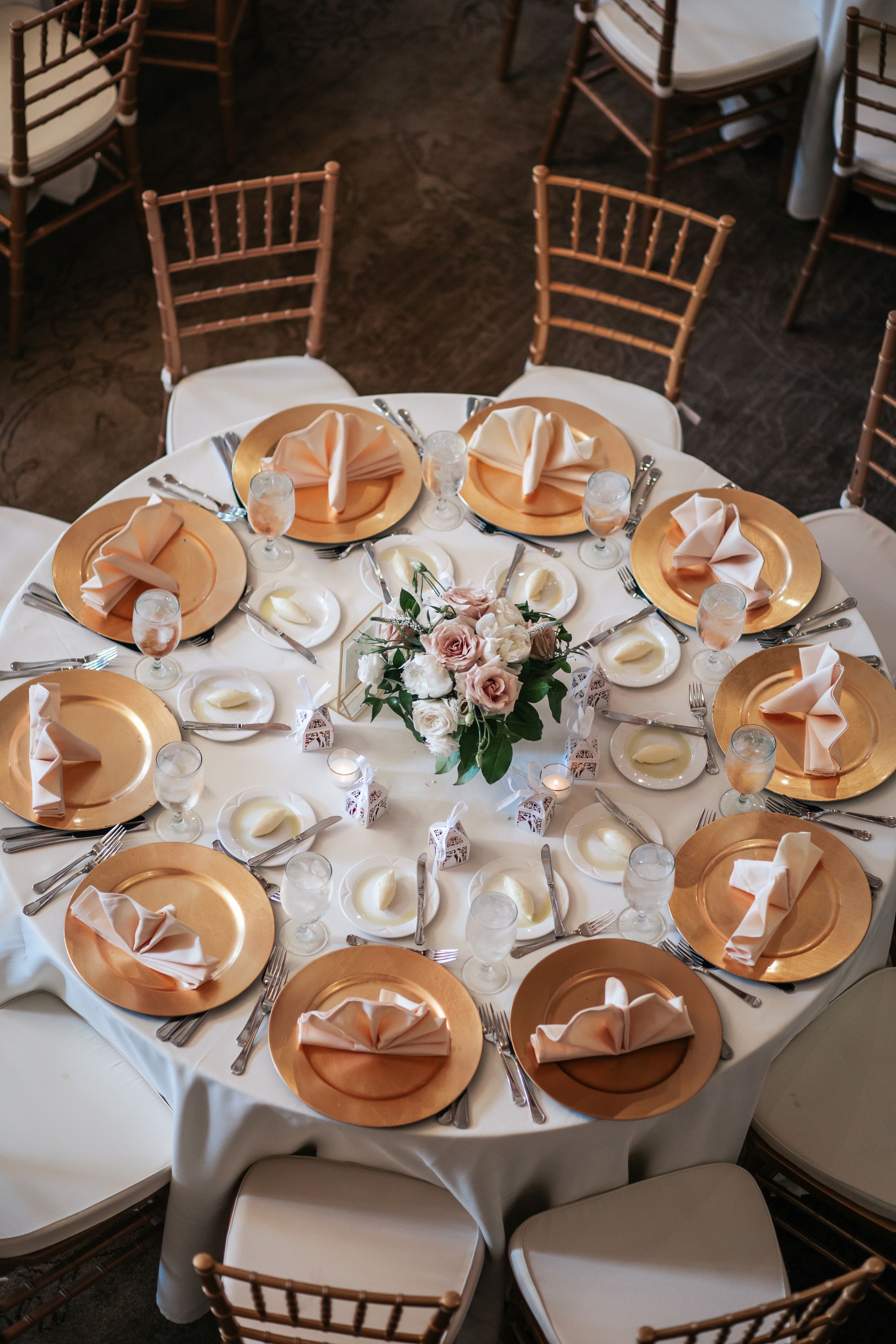 Elegant round dining tables set with rose gold charger plates, white linens, and delicate floral centerpieces at a formal event.