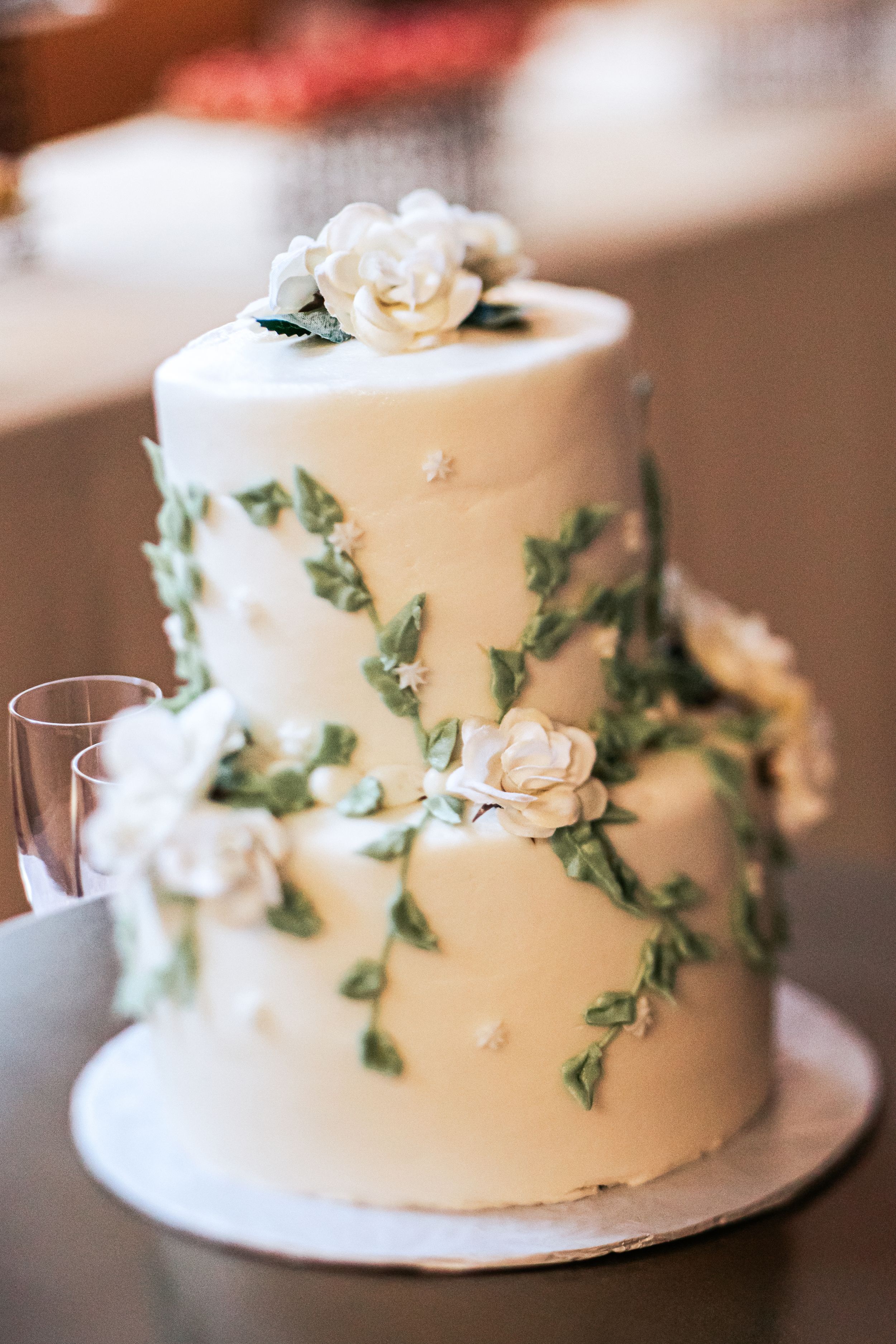Elegant two-tier white wedding cake decorated with delicate green vines and white sugar roses on display.
