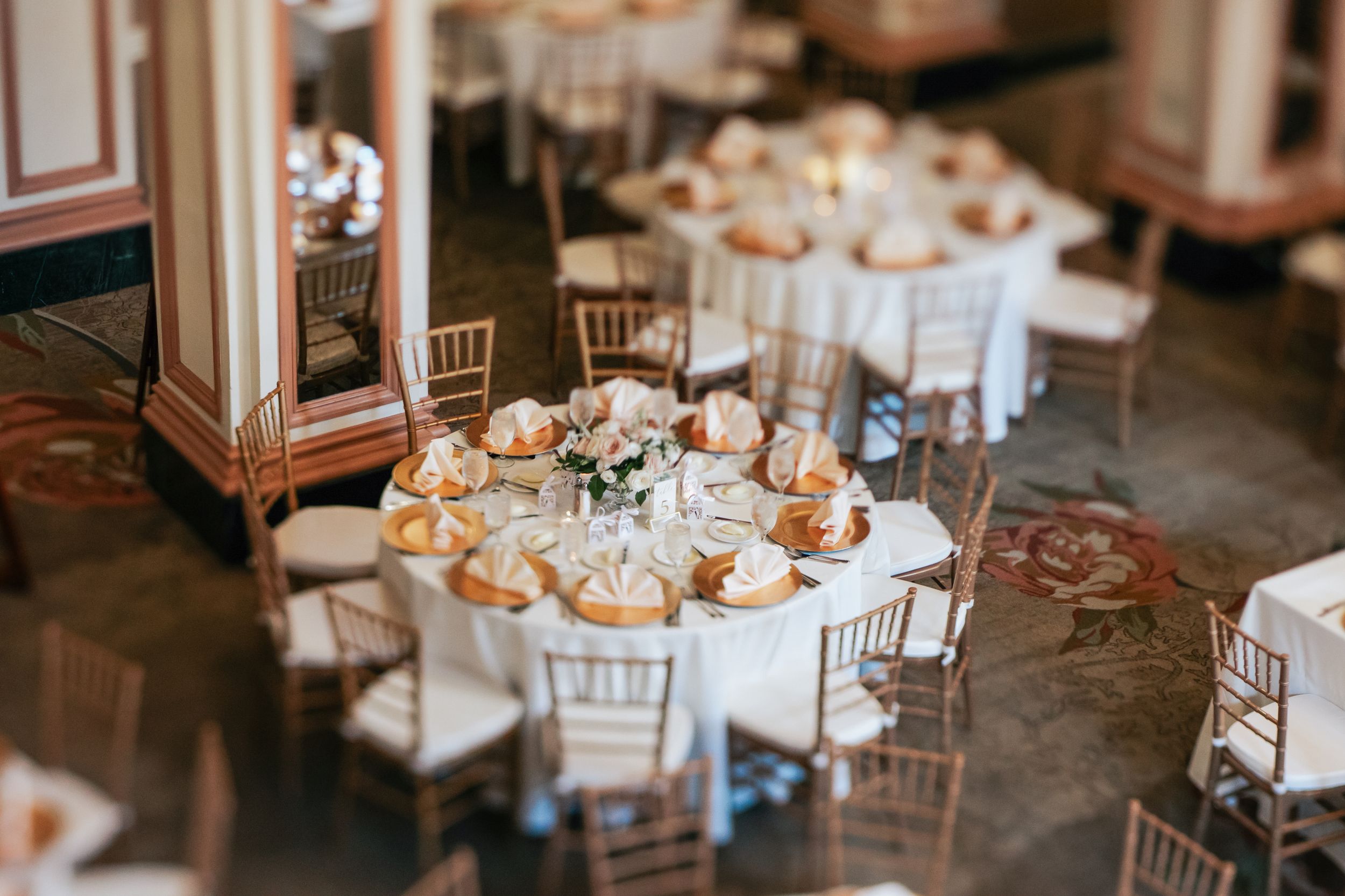 Elegant wedding reception tables decorated with white linens, floral centerpieces, and golden chiavari chairs.