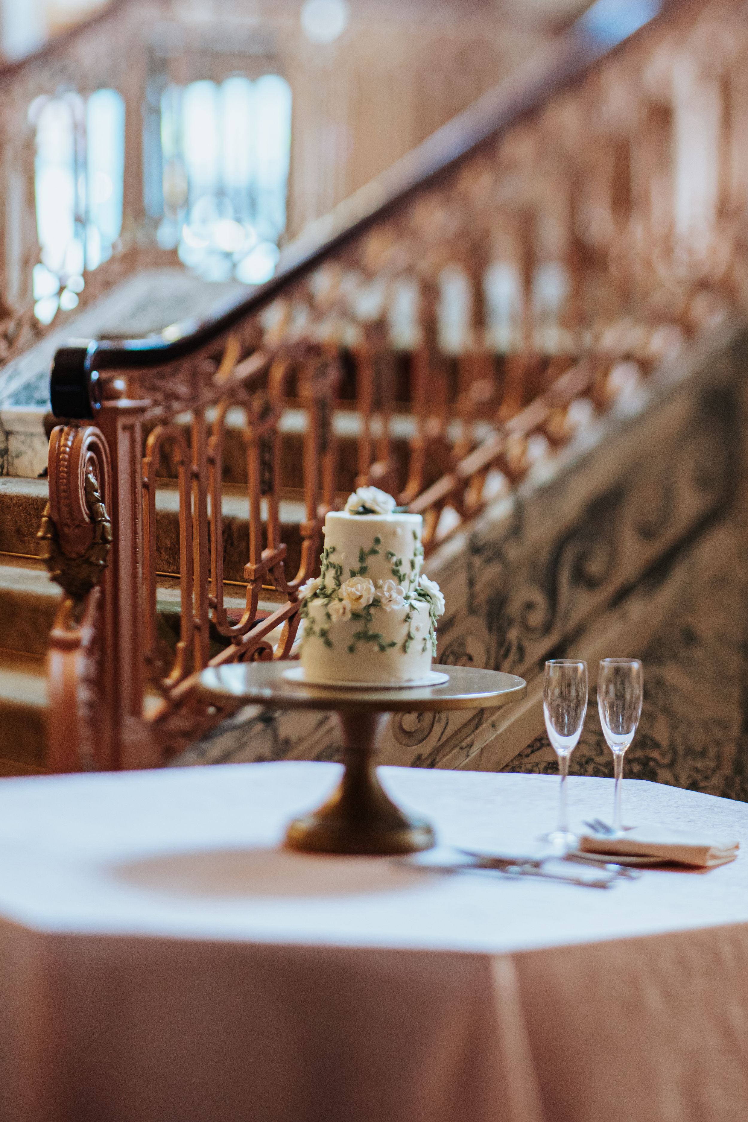 Elegant wedding reception table settings with champagne flutes and white tablecloths in warm lighting at a banquet hall.