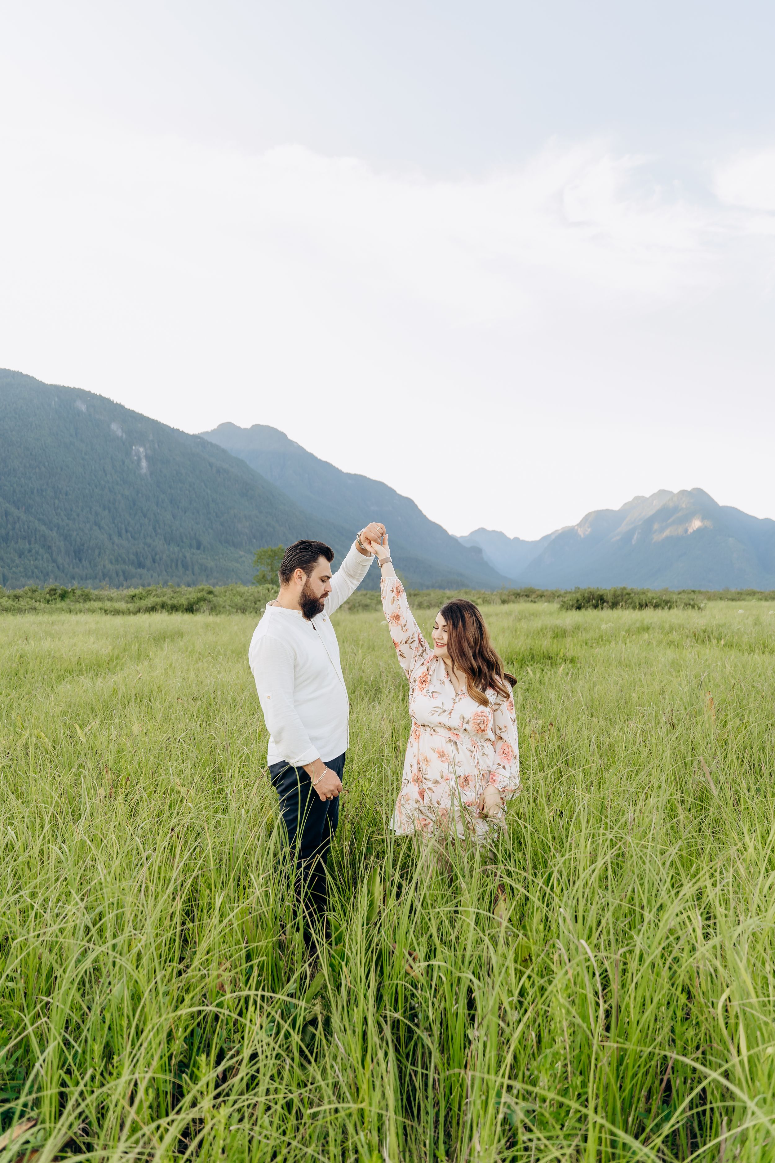 A couple dances together in a tall grass meadow with majestic mountains in the background.