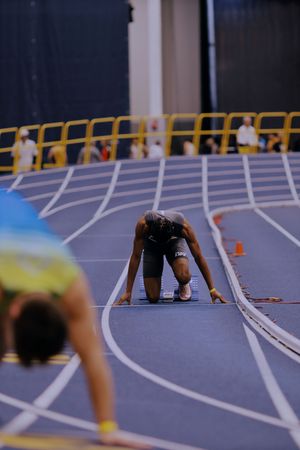 Athletes line up in starting position on a blue indoor track with white lane markings for a competitive race.