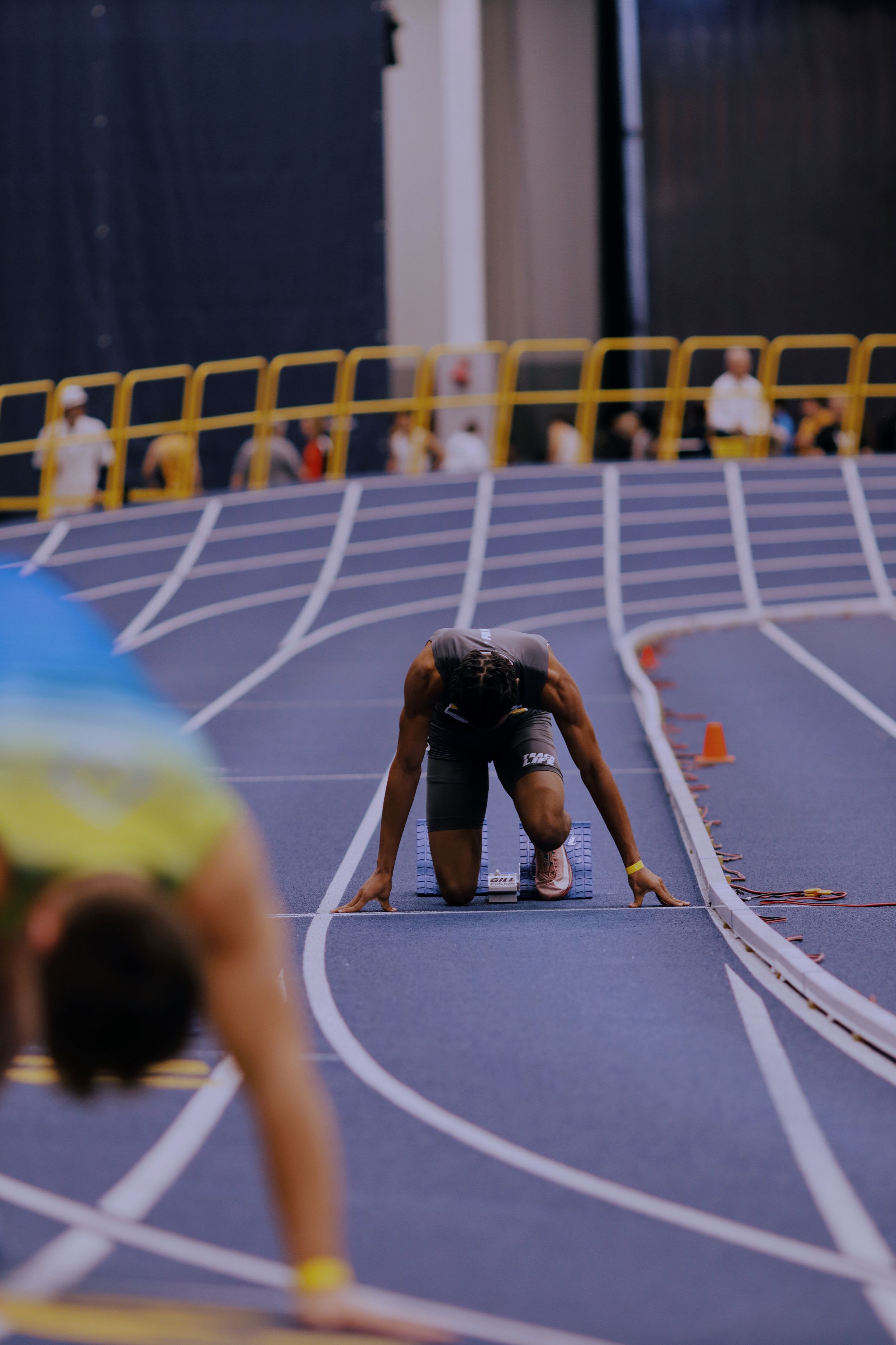 Athletes line up in starting position on a blue indoor track with white lane markings for a competitive race.