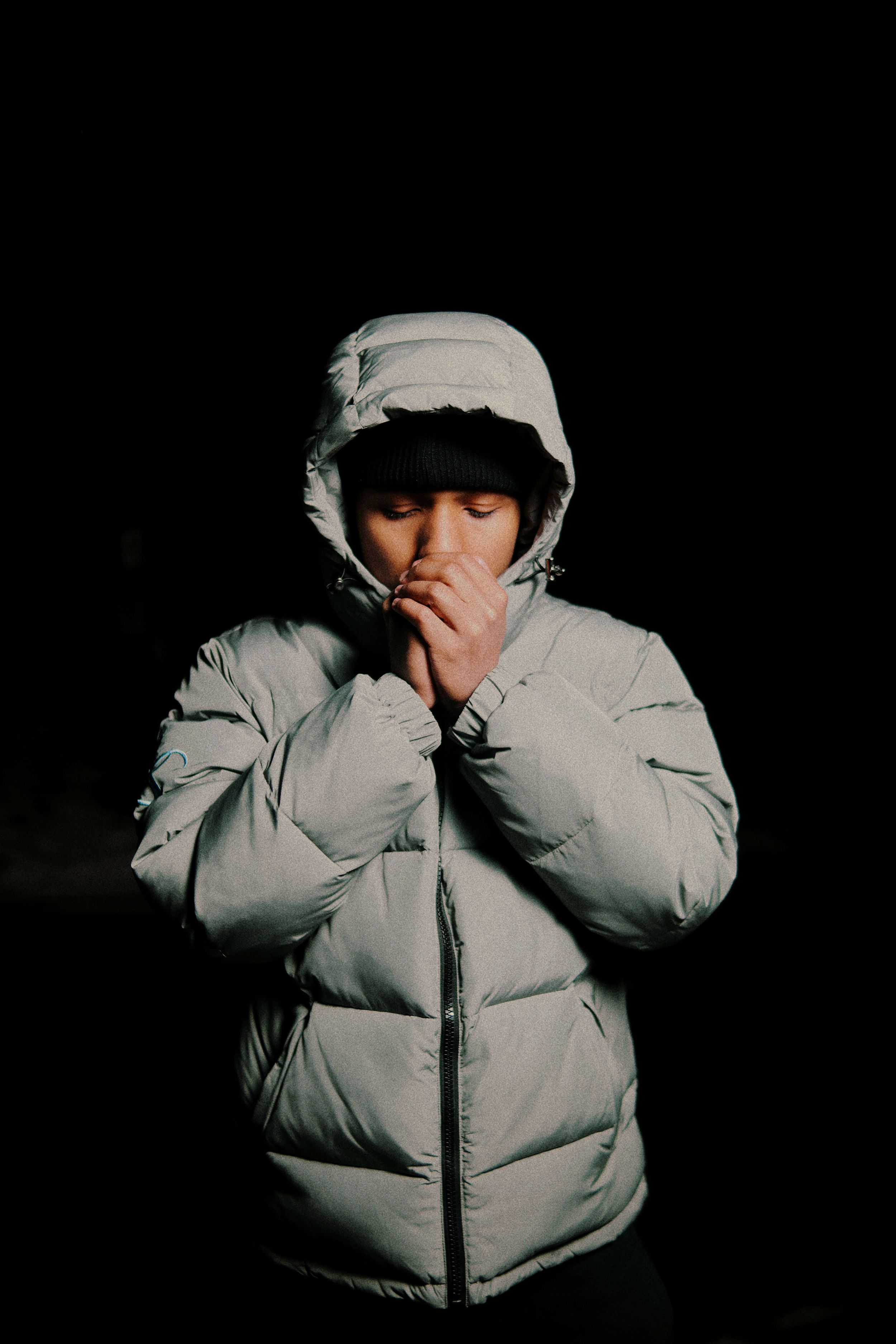 Person in white hooded puffer jacket warming hands against dark background in cold weather.