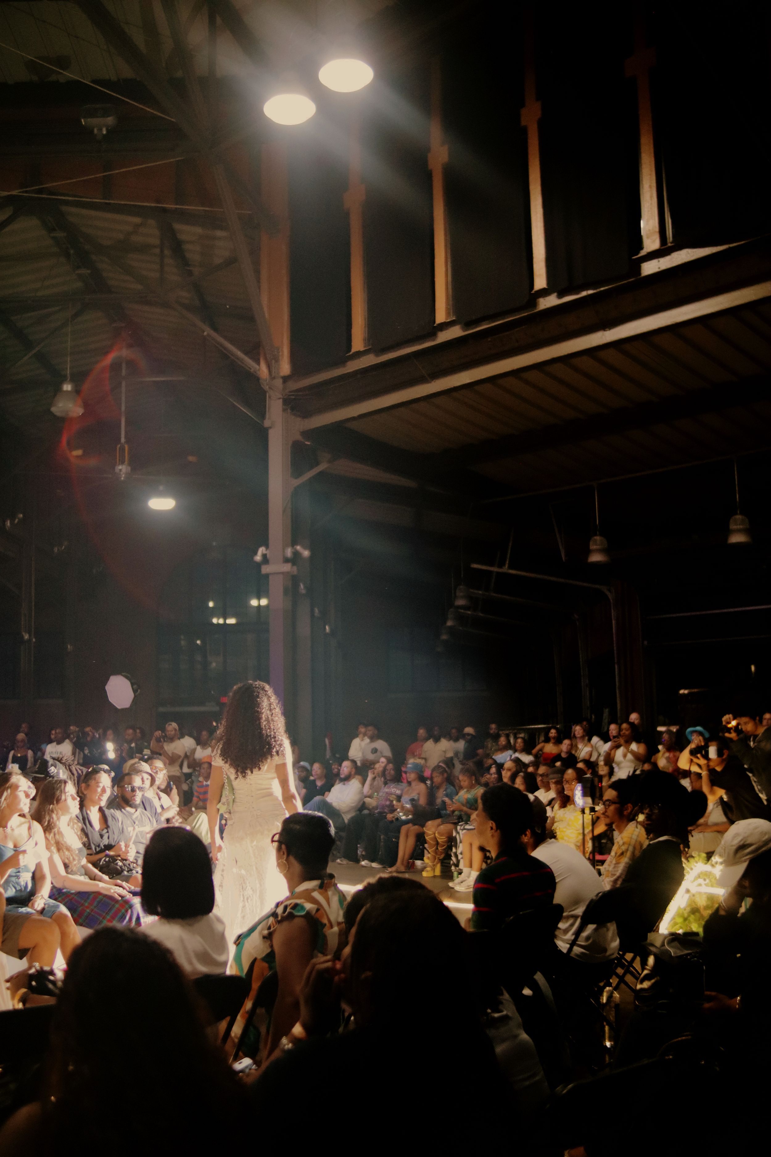 A dark concert venue with silhouetted crowd watching performers on stage illuminated by spotlights.